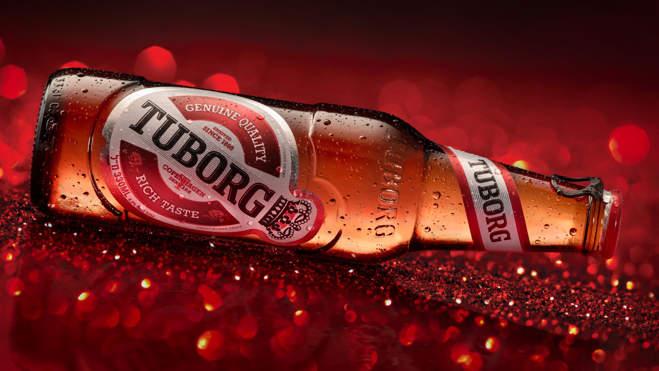 בקבוק בירה טובורג TUBORG קריר עם טיפות על רקע אדום כהה עם ניצנוצים בפוקוס סלקטיבי
