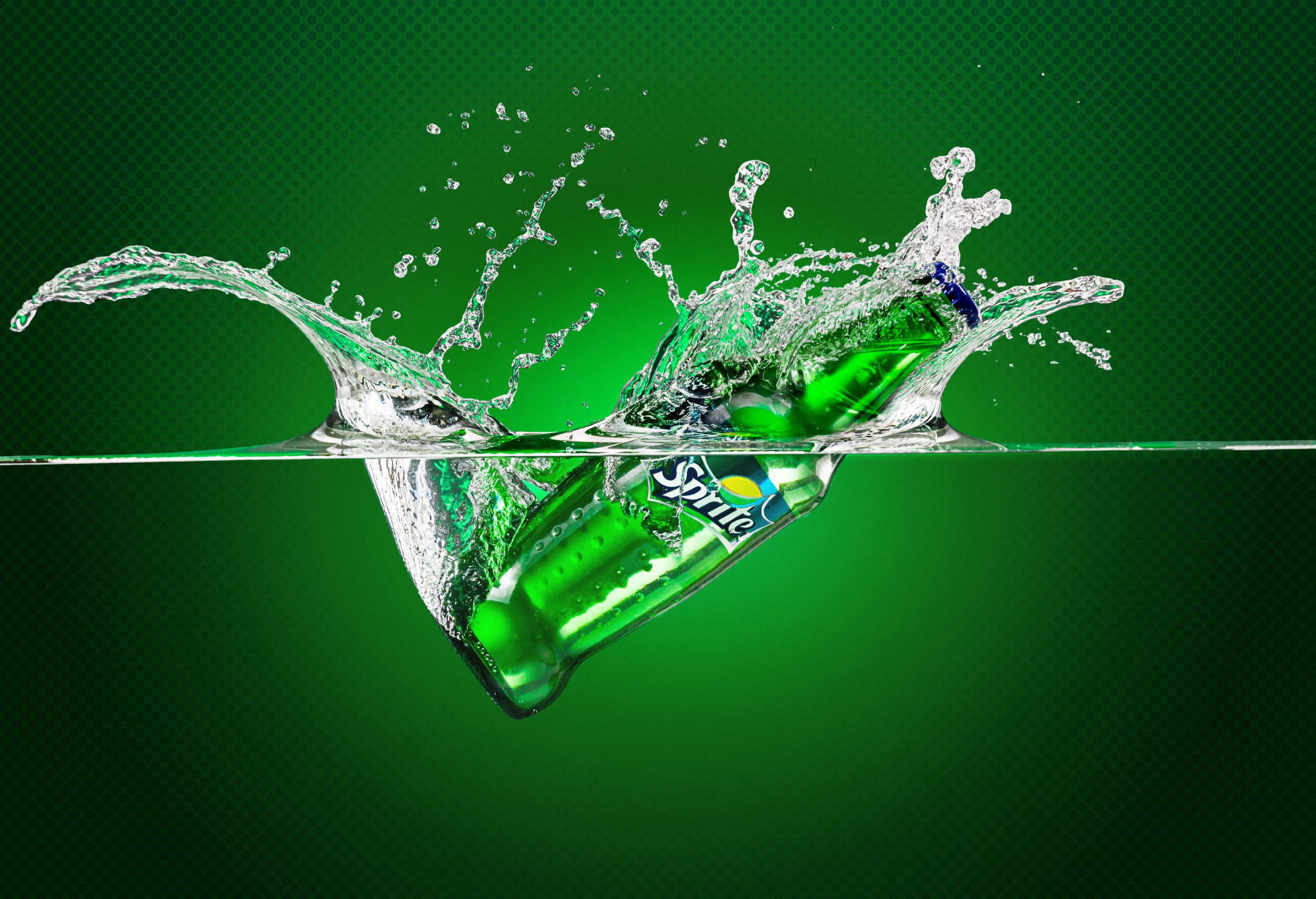 מודעה לספרייט בקבוק זכוכית נופל לתוך מים חצי מהבקבוק מחוץ למים וחצי שקוע עם שפריץ לכל עבר על רקע ירוק ולוגו SPRITE