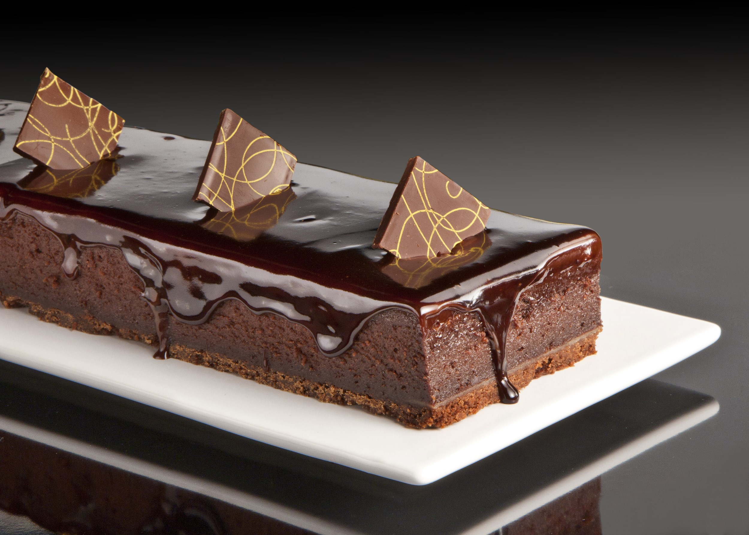 צילום עוגה שוקולד של רולדין על צלחת מלבנית לבנה על רקע שחור משתקף