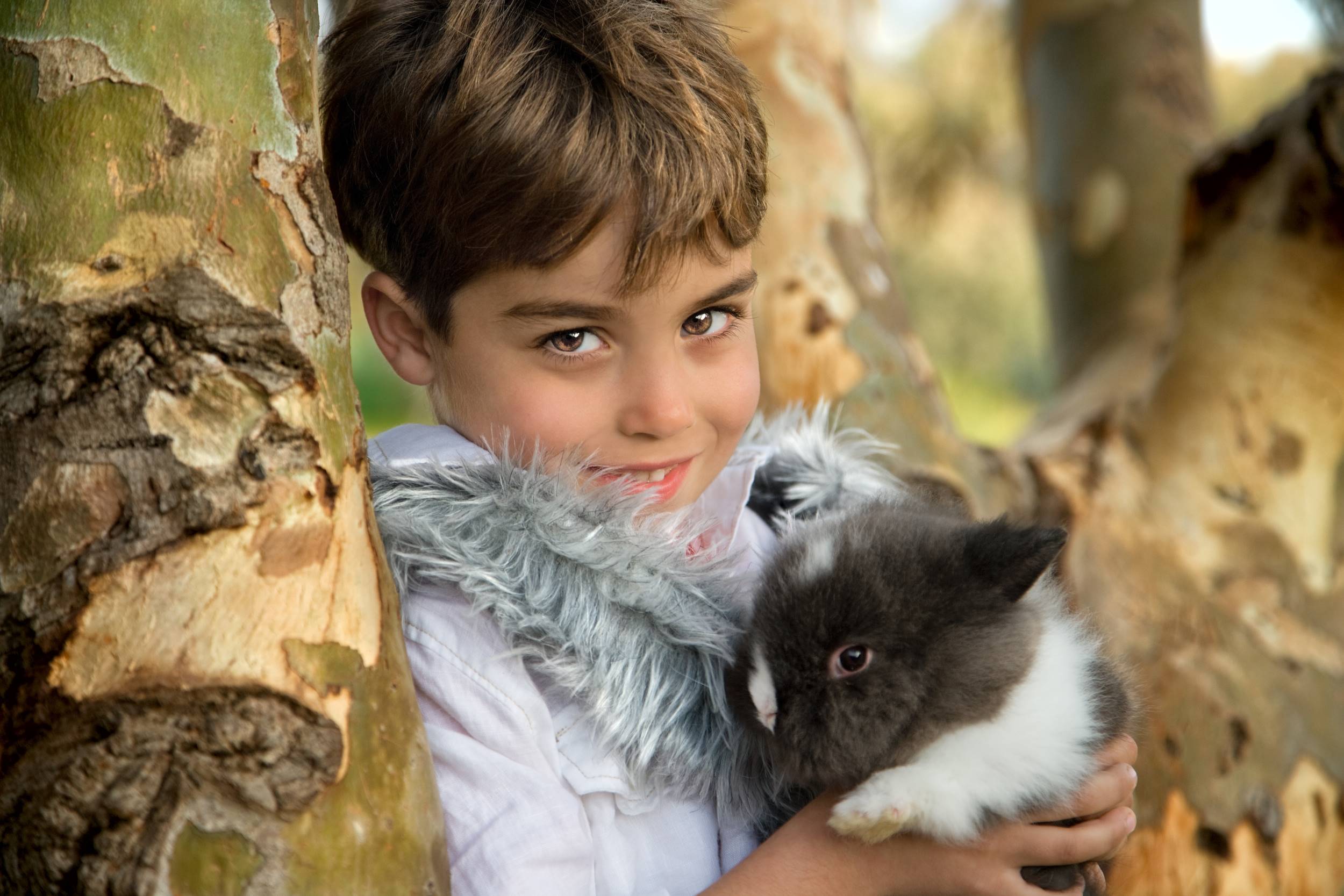 צילום ילד מחזיק ארנב עם עינים שקד מעיל לבן על עץ בטבע