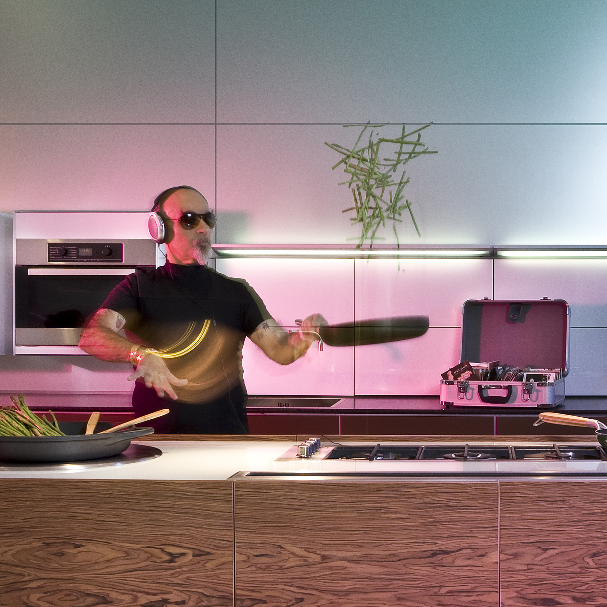 השף ישראל אהרוני מבשל במחבת שעועית ירוקה במטבח של סמל עם אוזניות וציוד די.ג'י מאחור. צולם ע'י סטודיו רייס עבור משרד פרסום סיגאווי