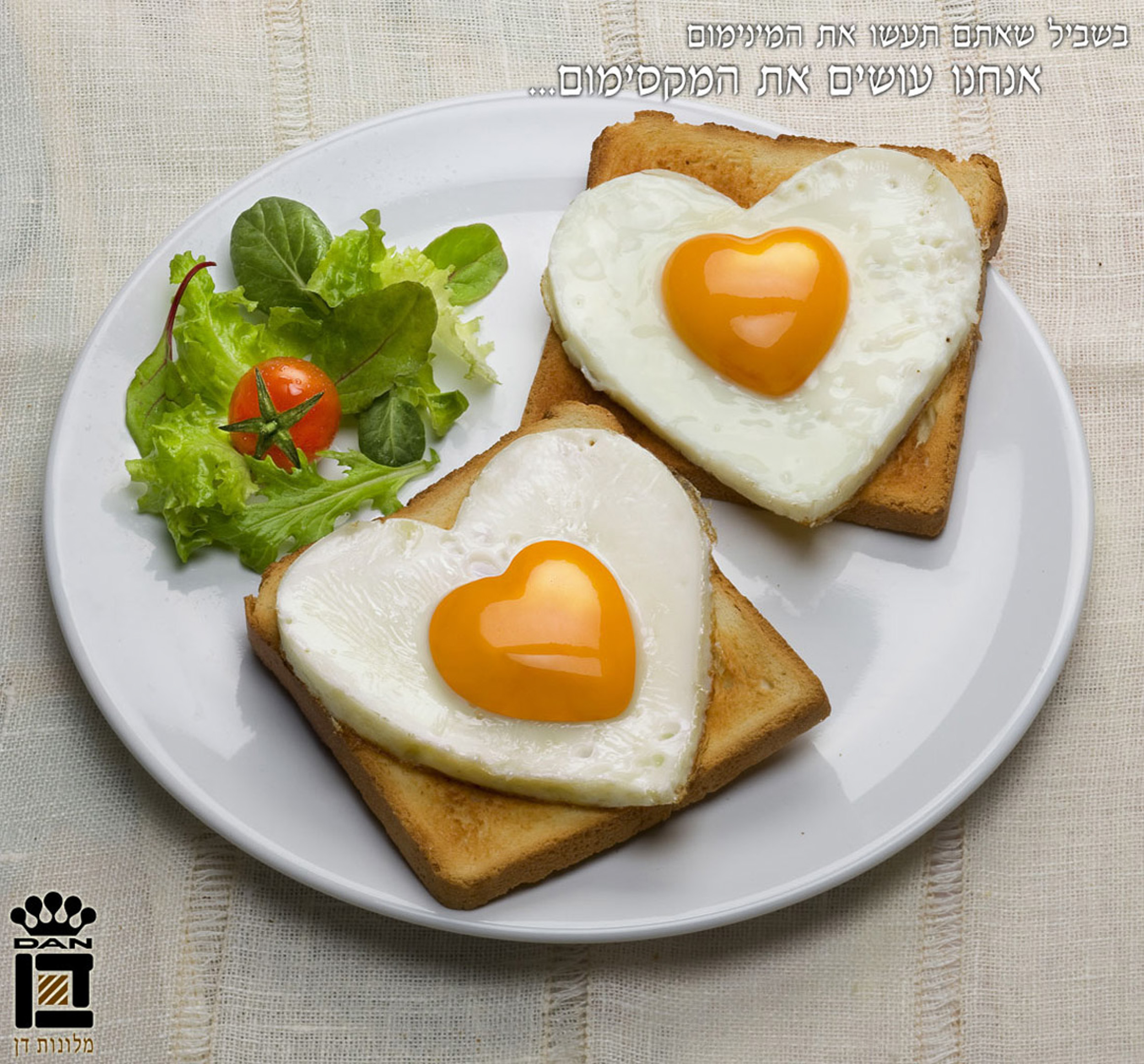 מודעה למלונות דן DAN HOTELS צלחת על מפה בז' עליה שני צנימי טוסט עם ביצי עין בצורת לב עם כמה עלים ירוקום ועגבניית שרי בצד. עם כיתוב בשביל שאתם תעשו את המינימום אנחנו עושים את המקסימום... ביצוע ע'י סטודיו רייס סטיילינג של נורית ברניצקי עבור משרד הפרסום באומן בר ריבנאי